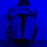 A person sits alone in a dark blue light, conveying feelings of sadness and solitude.