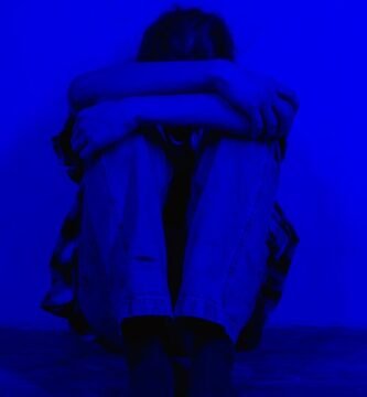 A person sits alone in a dark blue light, conveying feelings of sadness and solitude.