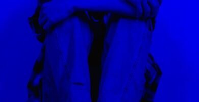 A person sits alone in a dark blue light, conveying feelings of sadness and solitude.